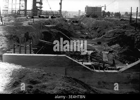 Nikolajewka, 1957. Slawjanskaja GRES. Ein detailliertes Archivfoto, das einen tiefen, ausgiebig ausgegrabenen Graben für den Wasserkanal des Kraftwerks SlavGRES oder die Fundamentstruktur zeigt. Dicke Betonwände sind bereits ausgegossen, während Holzschalungen und Stahlbewehrungen für weitere Bauschritte vorbereitet werden. Ein einsamer Arbeiter steht auf dem Betonbau auf der rechten Seite. Dieses komplexe, monochrome Vintage-Bild zeigt strenge Ingenieurarbeit und spiegelt die engagierte industrielle Arbeit, das Vorkriegsleben und die stetige Entwicklung im friedlichen Donbass wider. Stockfoto