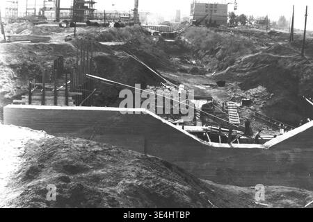 Nikolajewka, 1957. Slawjanskaja GRES. Ein alternativer Archivblick auf den tiefen Grabengraben an der belebten SlavGRES-Baustelle. Massive gegossene Betonwände bilden die Basis der Struktur, begleitet von komplexen Holzgerüsten und hervorstehenden Stahlverstärkungsstäben. Die Arbeiter navigieren durch das raue Gelände und die strukturellen Elemente innerhalb der Grube. Dieses fesselnde Vintage-Schwarzweiß-Foto dokumentiert die immense Größe der sowjetischen Ingenieurskunst und zeigt das tägliche Vorkriegsleben und harte industrielle Arbeit im friedlichen Donbass. Stockfoto
