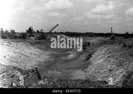 Nikolajewka, 1957. Slavyanskaja GRES Kraftwerksinfrastruktur massive Erdbewegung in einem atemberaubenden, weiten Landschaftsfoto. Mehrere schwere Schleppbagger befinden sich entlang der entfernten Kanten eines sehr langen, tiefen Grabens oder zukünftigen Wasserkanals, um aktiv den Boden zu graben und zu Formen. Der Himmel ist teilweise bewölkt über der riesigen Baustelle. Diese sehr eindrucksvolle Vintage-Aufnahme veranschaulicht die kolossale Größe der sowjetischen industriellen Erdwerke, die das fleißige Vorkriegsleben und die kontinuierliche Energieentwicklung im friedlichen Donbass widerspiegeln. Stockfoto