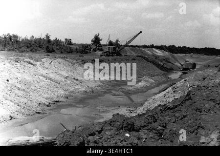 Nikolajewka, 1957. Slavyanskaja GRES Baustelle mit einem näheren Blick auf den Archivbereich der ausgedehnten Grabengrabung. Schwere mechanische Schleppbagger sind strategisch an den Sandbänken positioniert und entfernen große Erdmengen, um den tiefen Wasserkanal zu bilden. Lkw sind im Hintergrund deutlich sichtbar, was bei der massiven Logistik hilft. Dieses eindrucksvolle Vintage-Schwarzweiß-Bild unterstreicht die strenge Abhängigkeit von schweren Maschinen für monumentale Projekte, die harte Arbeit, das Vorkriegsleben und die schnelle Entwicklung im friedlichen Donbass einfangen. Stockfoto
