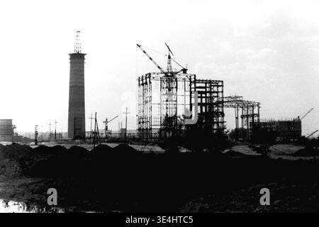 Nikolajewka, 1957. Slavyanskaja GRES Kraftwerkskomplex, der sich in einem beeindruckenden, breiten Silhouettenfoto wunderbar präsentiert. Der hohe, massive Betonschornstein steht stolz neben dem hochkomplizierten Stahlgerüst des Hauptgebäudes, auf dem ein aktiver Turmkran steht. Die dunkle, stark unebene Erdbaulandschaft füllt den Vordergrund vor einem sehr hellen Himmel. Dieses eindrucksvolle Vintage-Image dient als wahres Denkmal für die industriellen Ambitionen der Sowjetunion und spiegelt das fleißige Vorkriegsleben und das massive strukturelle Wachstum im friedlichen Donbass wider. Stockfoto