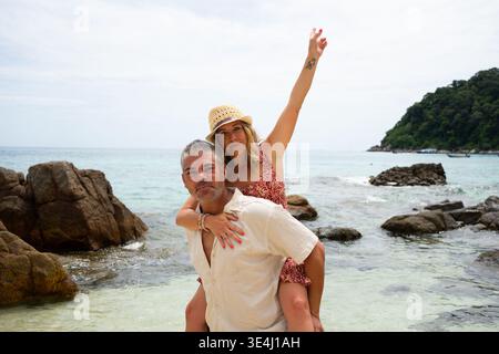 Glückliches Paar mit Huckepack am tropischen Strand, genießen den Sommerurlaub Stockfoto