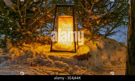 Leuchtende Laterne auf verschneiten Böden im Winterpark mit Tannen in der Abenddämmerung Stockfoto