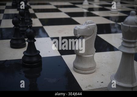 Ein mittleres, flaches Foto, das ein großes, öffentliches Schachbrett aus Stein auf dem Boden festlegt. Das Board selbst besteht aus strukturiertem, nassaussehendem schwarzem A Stockfoto