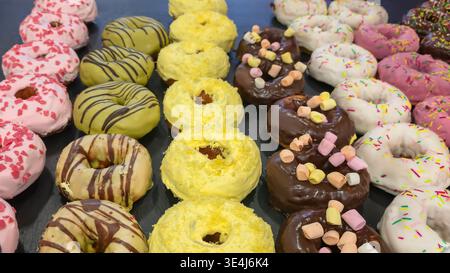 Eine Auswahl an bunten Donuts mit Glasur, Schokolade und dekorativen Streuseln. Eine Nahaufnahme von süßen Backwaren mit verschiedenen Geschmacksrichtungen und t Stockfoto