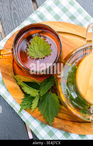 Blick von oben auf Kräuternessel Tee in einer Glasschale mit frischen Blättern auf einem Holzbrett, beruhigendes Entgiftungsgetränk für natürliche Pflege, Harnwegsunterstützung und Bala Stockfoto