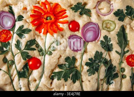 Blick von oben auf hausgemachte italienische Focaccia, dekoriert als Blumenkunst mit Tomaten, roten Zwiebeln, Petersilie und Erbsen, rustikales, handwerkliches Brot zum Backen oder Servieren. Stockfoto