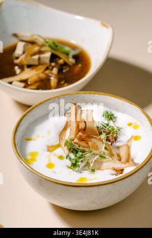 Zwei in Schüsseln servierte Suppen, Miso-Suppe mit Tofu und Pilzen sowie eine cremige Pilz- und Pastinakensuppe mit Mikrogrün und Öl. Stockfoto