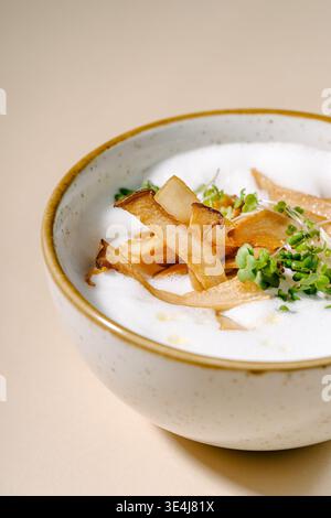 Creme aus Pilzen und Pastinaken, garniert mit gebratenen Pilzen und Pfifferlingen, luftigem Milchschaum, Congee, Mikrogrün und einem Hauch Muskatnuss in einer Resta Stockfoto
