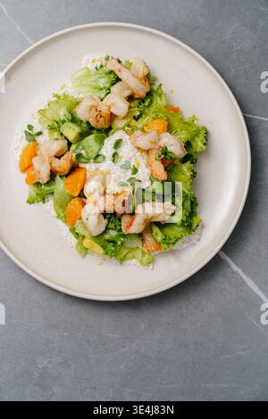 Blick von oben auf Salat mit frittierten Tigergarnelen, Orangensegmenten, Avocado, knusprigem Salat und Mikrogrün, garniert mit cremiger Zitronensauce und Zitronenschale auf A Stockfoto