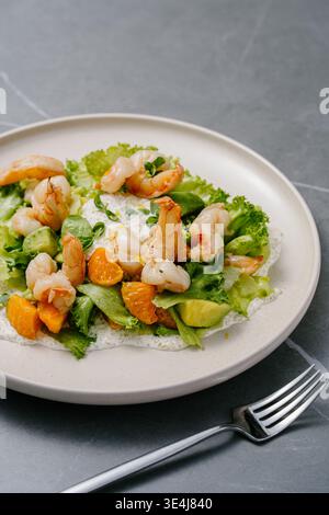 Frischer Salat mit frittierten Tigergarnelen, Orangensegmenten, Avocado, knusprigem Salat und Mikrogrün, serviert mit cremiger Zitronensauce und heller Zitronenschale Stockfoto