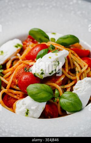 Close-up von Spaghetti mit Kirschtomaten und cremiger Burrata, in Olivenöl und Knoblauch geschüttet, mit frischem Basilikum, Salz und schwarzem Pfeffer abgerundet, servieren Stockfoto