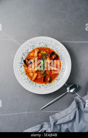 Blick von oben auf Bouillabaisse Meeresfrüchte-Eintopf mit Garnelen, Muscheln in Muscheln, Tintenfischringe und Fischfilet in Tomaten-Safranbrühe, mit Kräutern, Zitrone und pepp Stockfoto