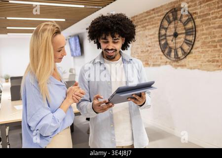 Lateinischer Mann und weibliche Kollegin prüfen Daten auf einem Tablet in einem modernen Coworking-Büro und diskutieren Projektideen und Teamarbeit in einem hellen, offenen Design Stockfoto
