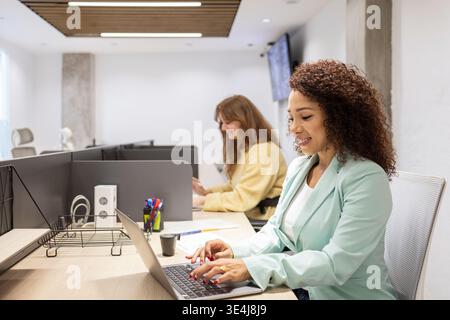 Verschiedene Kollegen konzentrieren sich auf Notebooks in einem hellen, modernen Coworking-Büro, das Teamarbeit, Produktivität und geschäftliche Zusammenarbeit in einem offenen Arbeitsumfeld zeigt Stockfoto
