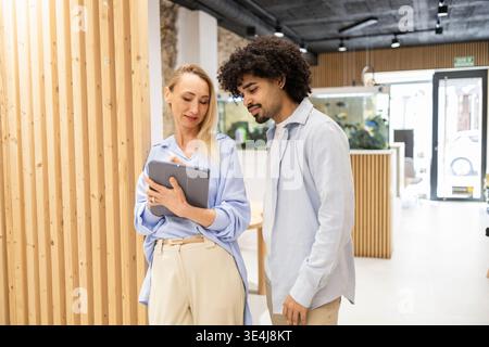 Modernes Coworking-Team in einem hellen Büro prüfen ein Lateinmann und eine Kollegin gemeinsam ein Tablet, diskutieren ein Projekt und planen die nächsten Schritte Stockfoto