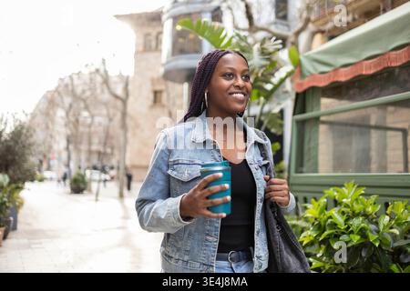 Eine Frau schlendert entlang der pulsierenden Diagonalstraße im Stadtteil Gracia von Barcelona, Spanien, und genießt einen ungezwungenen Lebensstil und hält eine Tasse Cof Stockfoto