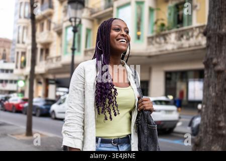 Eine junge Frau mit lila geflochtenen Haaren läuft selbstbewusst die Diagonal Street im lebhaften Stadtteil Gracia von Barcelona, Spanien, hinunter und genießt ein Leben Stockfoto