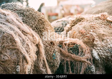 Nahaufnahme eines großen Anhäufens von Fischernetzen in einem Hafen, verwickelte Seile und Maschen in weichem Licht, mit verwitterter Textur, Ausrüstung für die maritime Industrie, Stockfoto