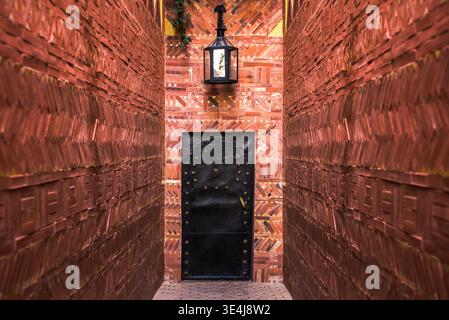 Erstaunliche, schöne und sehr detaillierte Lehm-Ziegelwand-Textur, die eine traditionelle schwarze Tür und Laterne in einem schmalen Durchgang, Marrakesch, Marokko, umrahmt Stockfoto