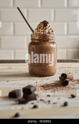 Lifestyle-Nahaufnahme mit dekadentem Kaffee in einem klaren recycelten Glas, gekrönt mit einem dicken Wirbel Schlagsahne, mit Kakao und s bestäubt Stockfoto