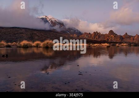Ein atemberaubender Winterblick auf den Teide, Teneriffa, die Kanarischen Inseln, umgeben von Wolken, mit seiner Reflexion, die wunderschön in einem ruhigen Gewässer gefangen ist. Stockfoto