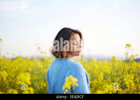 Porträt einer Frau, die friedlich in einem Feld aus leuchtenden gelben Blumen steht, die das Wesen des Frühlings und die Schönheit der Natur verkörpert, unter einer klaren, ruhigen Atmosphäre Stockfoto