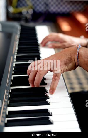 Eine Person unbekannter ethnischer Herkunft spielt zu Hause Klavier, wobei die Hände über den Tasten sichtbar sind. Die Szene findet tagsüber statt und betont die Arbeit aus Stockfoto