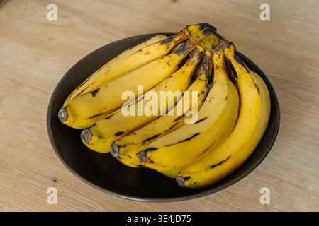 Reifer Bananenbunch Auf Schwarzer Platte, Holztisch, Küchenvorbereitung Für Morning Smoothie, Weiches Natürlich Stockfoto