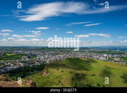 Panoramablick über Edinburgh vom Arthur's Seat und den Salisbury Crags, der das historische Stadtbild, die sanften grünen Hügel, die Küste und das helle blau zeigt Stockfoto