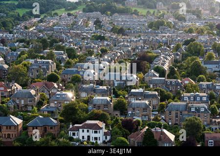 Blick aus der Vogelperspektive auf ein Wohnviertel von Edinburgh mit historischen Steinhäusern, grünen Gärten und Terrassenstraßen, die auf einem grünen Hügel klettern Stockfoto