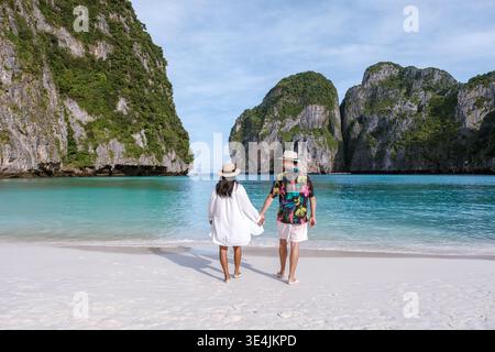 Ein paar Spaziergänge Hand in Hand an einem unberührten Strand in Koh Phi Phi, Thailand, umgeben von hohen Kalksteinklippen und kristallklarem türkisfarbenem Wasser. Stockfoto