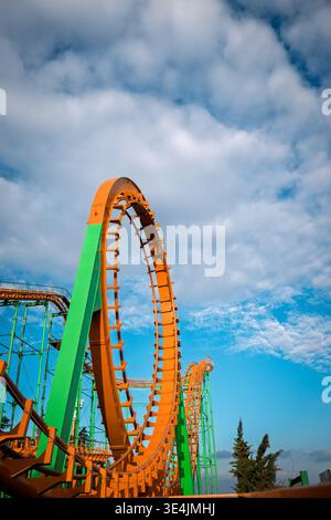 Flacher Blickwinkel auf eine leuchtende orange Achterbahnschleife und grüne Stützen unter einem dramatischen Himmel Stockfoto