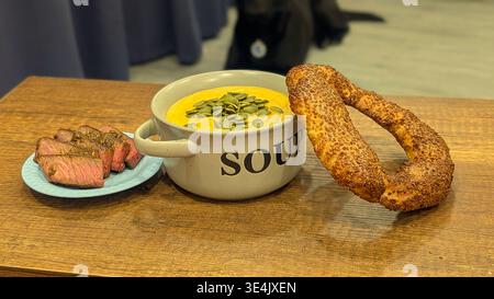 Ein Hochwinkelfoto einer herzhaften Mahlzeit mit einer Schüssel cremiger Kürbissuppe, garniert mit grünen Samen. Serviert mit saftigen Scheiben von mittelseltenem Rindfleisch Stockfoto