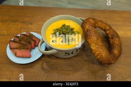 Ein Hochwinkelfoto einer herzhaften Mahlzeit mit einer Schüssel cremiger Kürbissuppe, garniert mit grünen Samen. Serviert mit saftigen Scheiben von mittelseltenem Rindfleisch Stockfoto