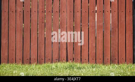 Roter Holzzaun, der eine Grenze in einem grünen Garten bildet Stockfoto