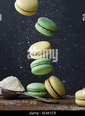 Dieses fesselnde Bild zeigt eine Kaskade lebendiger Macarons in hellen Gelb- und frischen Grüntönen, von denen einige in Bewegung schwebt, als ob sie fallen oder ein Bein wären Stockfoto