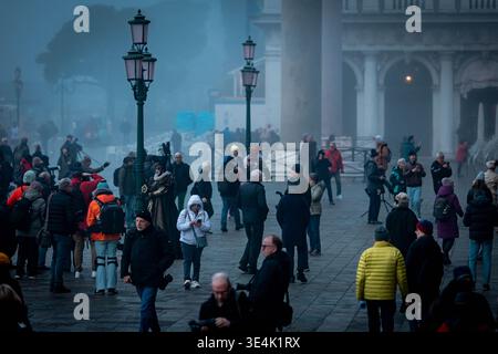 Venedig, Italien - 13. Februar 2026: Menschenmassen in bunten Kostümen und Masken versammeln sich während des Karnevals von Venedig mit historischem B auf einem nebeligen Platz Stockfoto