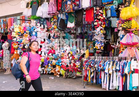Mexikanische Frau, die vor einem kleinen Laden mit vielen Waren in der Innenstadt von Merida, Yucatan, Mexiko läuft Stockfoto