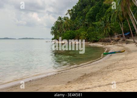 Coconut Beach, Port Barton, Philippinen – 8. April 2024: Ein Kajak ruht auf dem Sand neben ruhigem Meerwasser entlang einer palmengesäumten tropischen Küste. Stockfoto