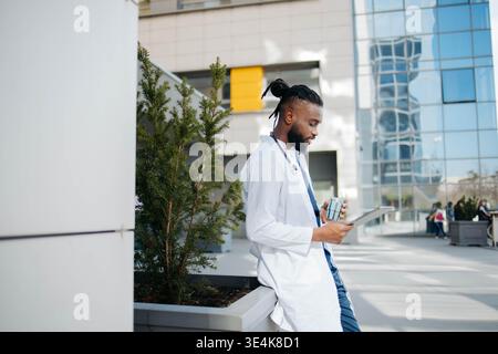 Digitales Notizblock liegt in der Hand. Der junge schwarze Doktor ist auf dem Flur Stockfoto