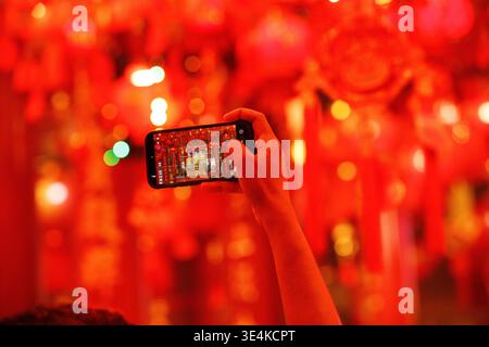 Männliche Hand, die ein Smartphone hält, macht Fotos von der Schrein-Ausstellung, Nahaufnahme, Tiefwinkelansicht, am Mangkon-Tempel. Stockfoto