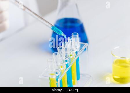 Nahaufnahme der Pipette, die blaue Flüssigkeit in leere Reagenzgläser tropft, Laborversuch und präziser chemischer Testprozess Stockfoto