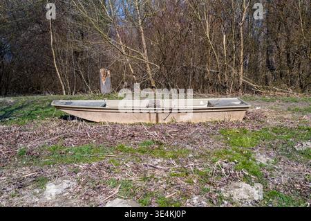 Ein verlassenes Boot liegt am Ufer, das dem Verfall überlassen ist. Das Boot wird nicht mehr genutzt, und die Umgebung ist mit Unkraut und Gras bewachsen. Stockfoto