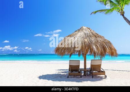 Luxuriöse Strandszene mit Sonnenschirm und Liegestühlen auf weißem Sand und türkisfarbenem Meer in Punta Cana, Dominikanische Republik. Ideal für Reisen, Resorts und Stockfoto