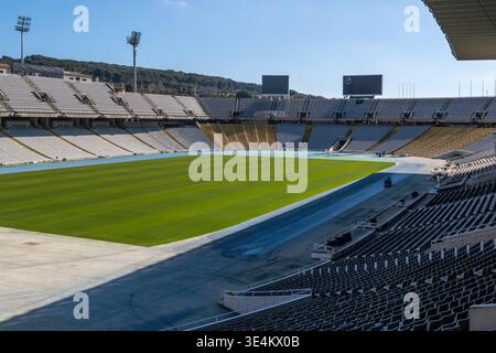 Schräge Aussicht über ein großes leeres Stadion in Barcelona mit grünem Feld, blauem Track, Sitzreihen und Anzeigetafeln unter klarem Himmel. Stockfoto