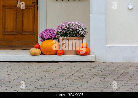 Herbstdekoration mit Kürbissen und Chrysanthemen auf einer Steintür in der Nähe einer Holztür, gemütliches saisonales Erntekonzept. Stockfoto