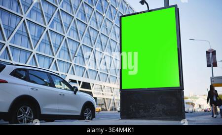 Eine leere vertikale grüne Plakatwand in einer Stadtstraße mit modernem Gebäude und Verkehr Stockfoto