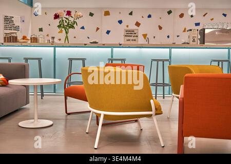 Modernes Café mit leuchtendem Senfgelb und orange gepolsterten Sesseln mit weißen und roten Metallrahmen, die um einen kleinen weißen Rahmen angeordnet sind Stockfoto