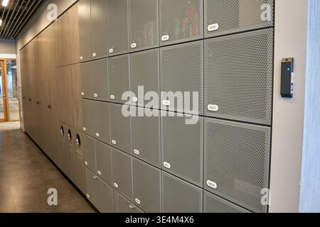 Ein moderner Innenraum mit einer Wand aus grauen, perforierten Metallschränken mit Gittertüren und weißen Kennzeichnungsschildern, die in A angeordnet sind Stockfoto